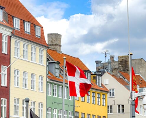 Dansk flagg foran fargerike bygninger i Nyhavn i København