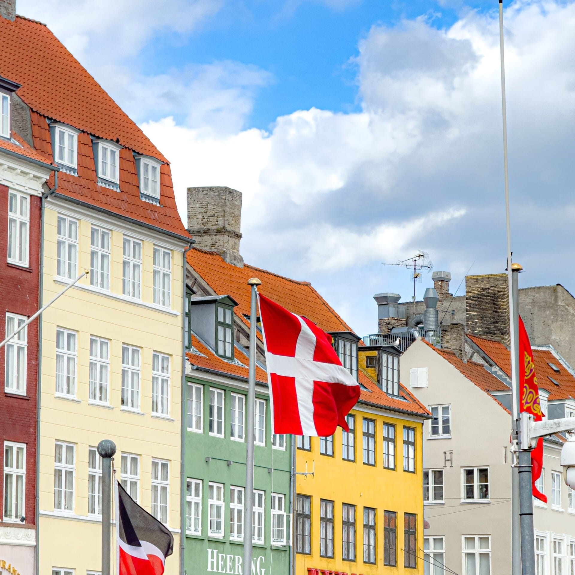 Dansk flagg foran fargerike bygninger i Nyhavn i København